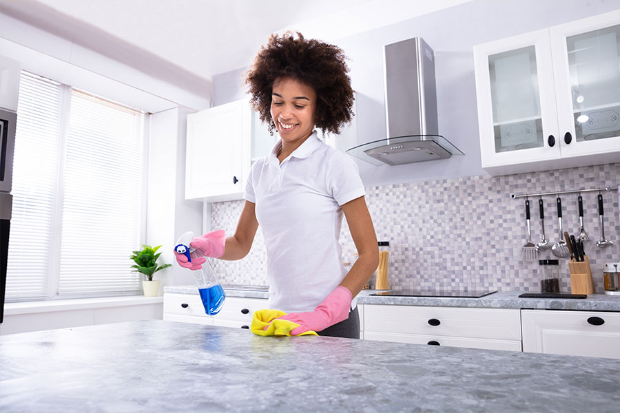 A young maid in a white shirt and pink gloves using a eco-friendly cleaning solution on a kitchen countertop in St. Charles and St. Louis, MO.