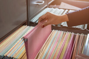 A person wearing a long black top grabbing a pile folder that is organized in metal file containers in an office in St. Charles, MO.