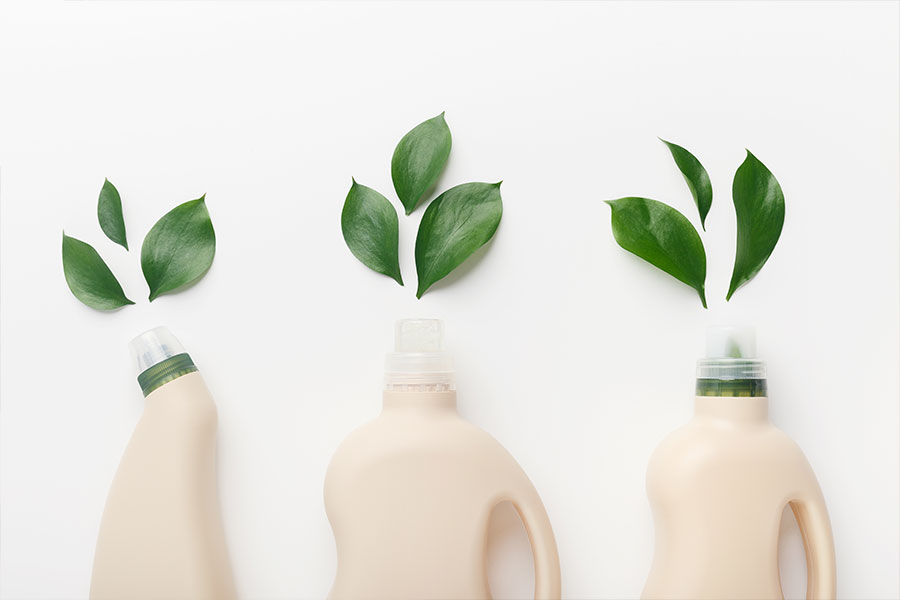 A frontal image of three eco-friendly cleaning products laying on a white table in St. Charles, MO with green leaves lying in front of the bottle.