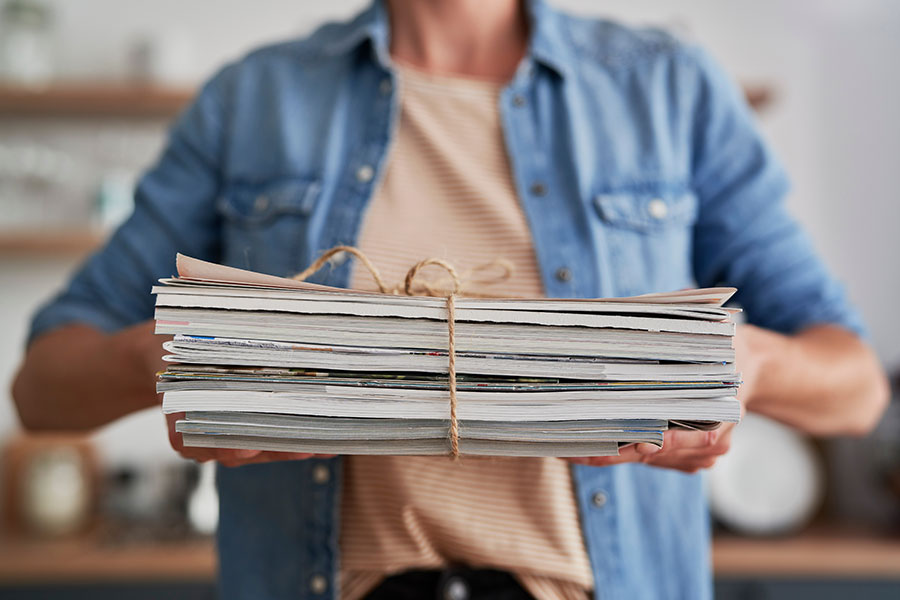 A person holding old newspapers, articles, and magazines that are needing to be recycled to avoid clutter in St. Charles, MO.