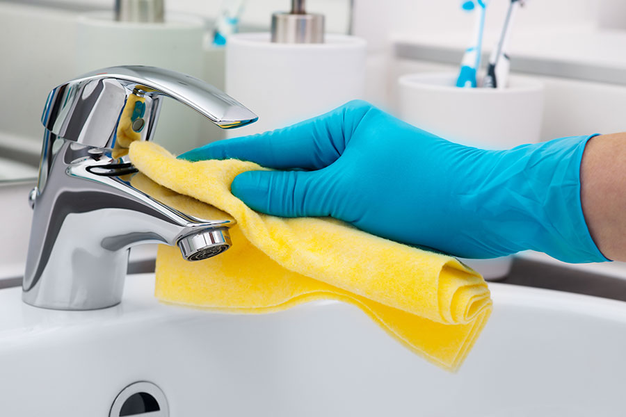 A professional maid cleaning a faucet in a residential bathroom in St, Charles, MO that is included in a general cleaning package.