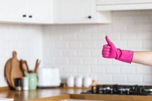 A maid in St. Charles, MO wearing a pink rubber glove holding a thumbs-up sign with a clean residential kitchen in the background.