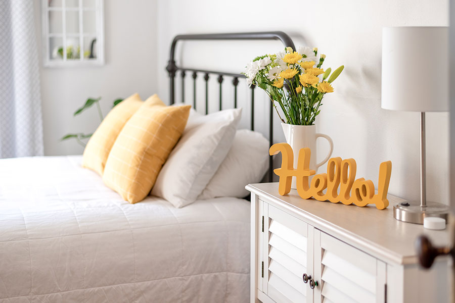 A clean bedroom in St. Charles, MO with a white comforter and white and yellow pillows that has been kept clean due to our maid services.