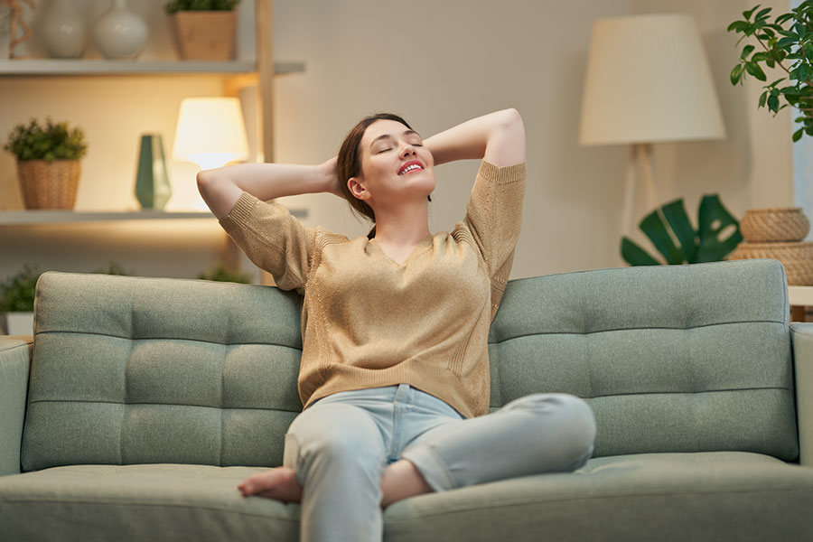 A young brunette in jeans and a yellow shirt relaxing on her green living room sofa in O’Fallon, MO, benefiting from a professional cleaning service.