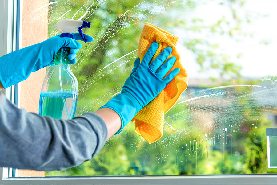 A professional maid using a window cleaning solution and a yellow rag to clean the window of a residential or commercial residence in Earth City, MO for spring cleaning.