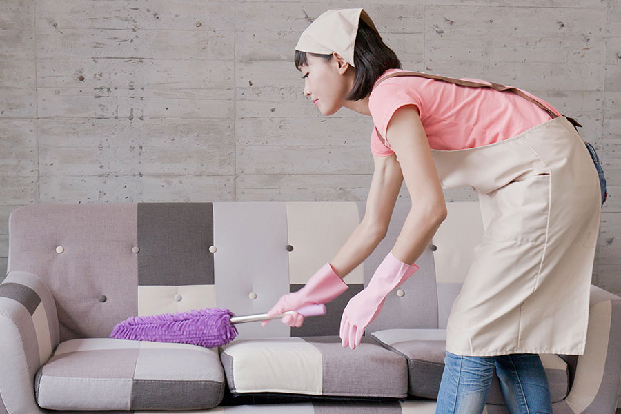 A professional housekeeper that is dusting off the couch in a residential home in Chesterfield, MO.