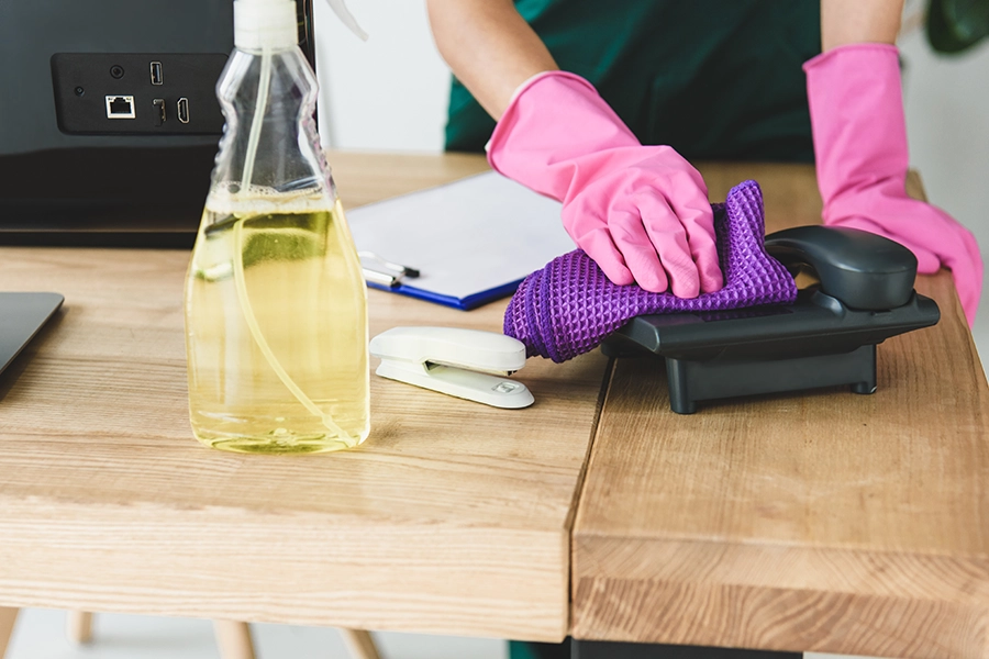 Up close picture of a woman with pink gloves using a cleaning product to sanitize office phone in Chesterfield, MO.